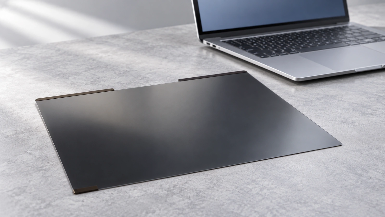 A thin dark filter with two separated top strips lies beside an open silver laptop.