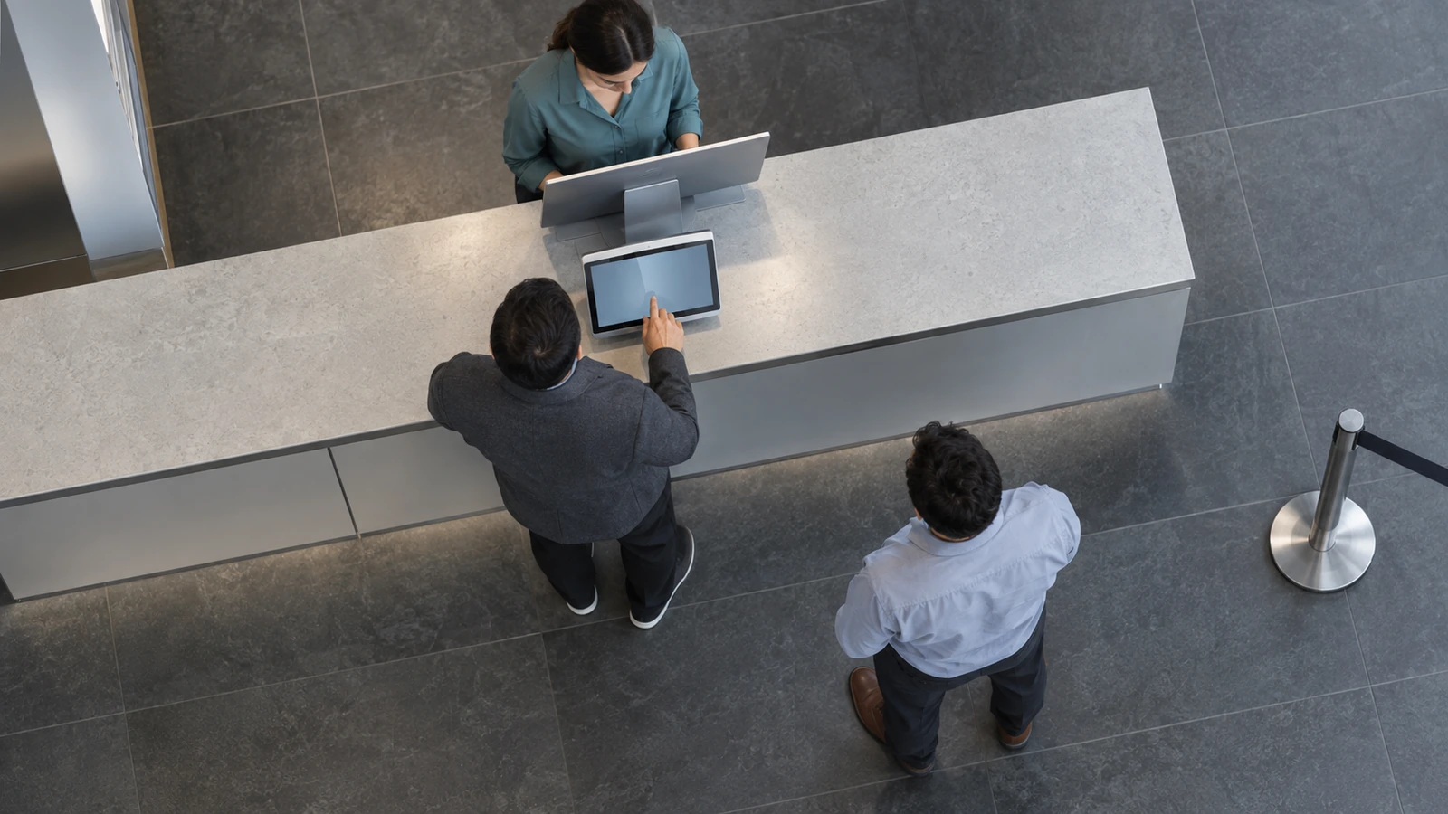 A retail counter showing an operator behind a monitor, a customer at a touchscreen and another person waiting nearby.