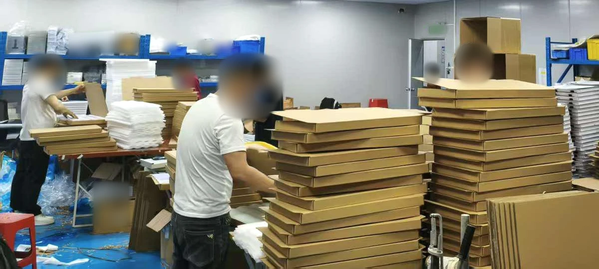 People organize open cardboard boxes, foam sheets and packaging materials at worktables.