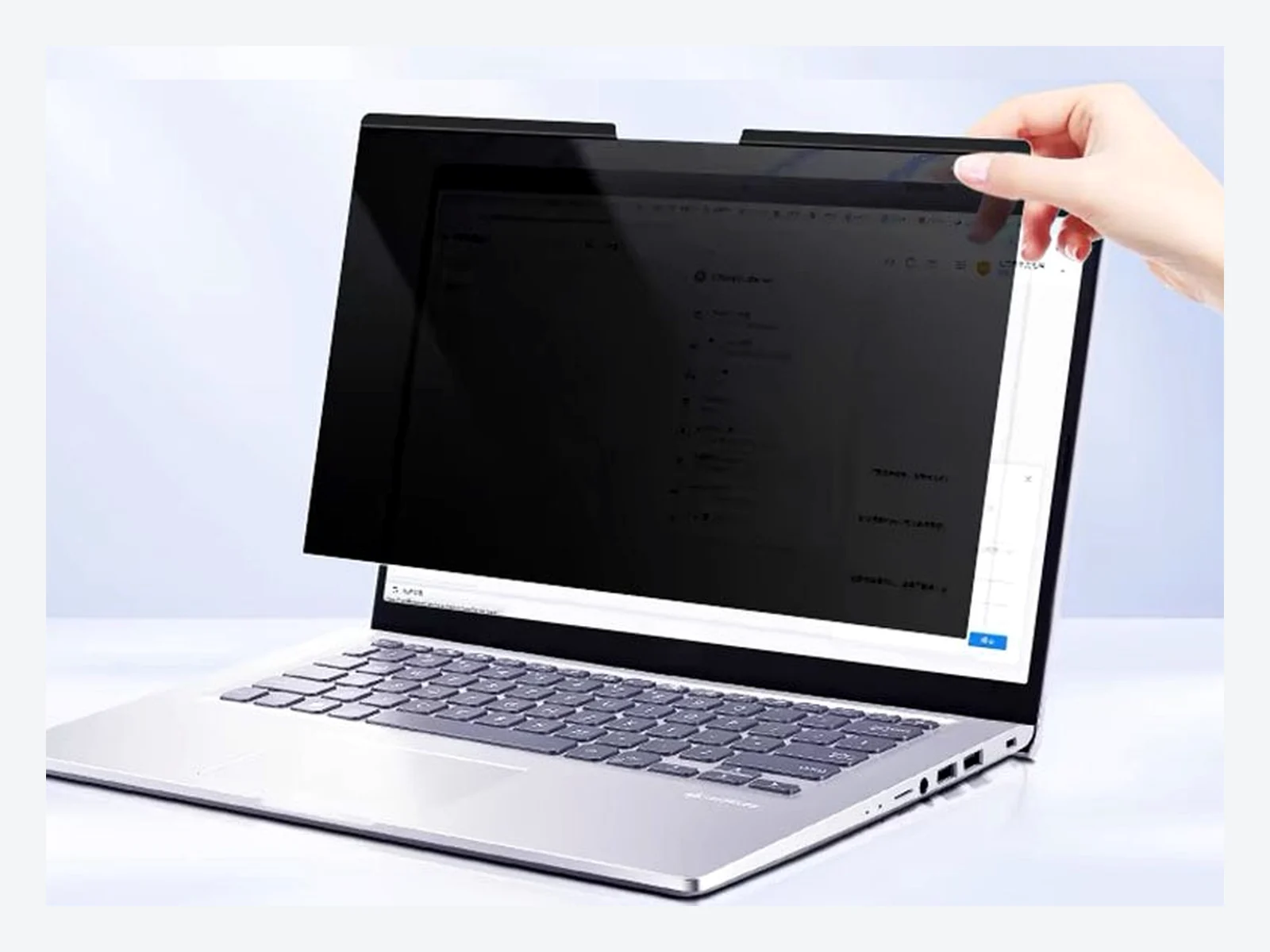 Hand aligning a magnetic privacy filter with the top edge of a laptop display