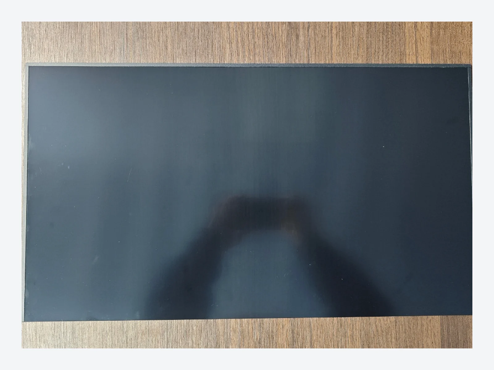 Rectangular dark monitor privacy filter laid flat on a wood surface