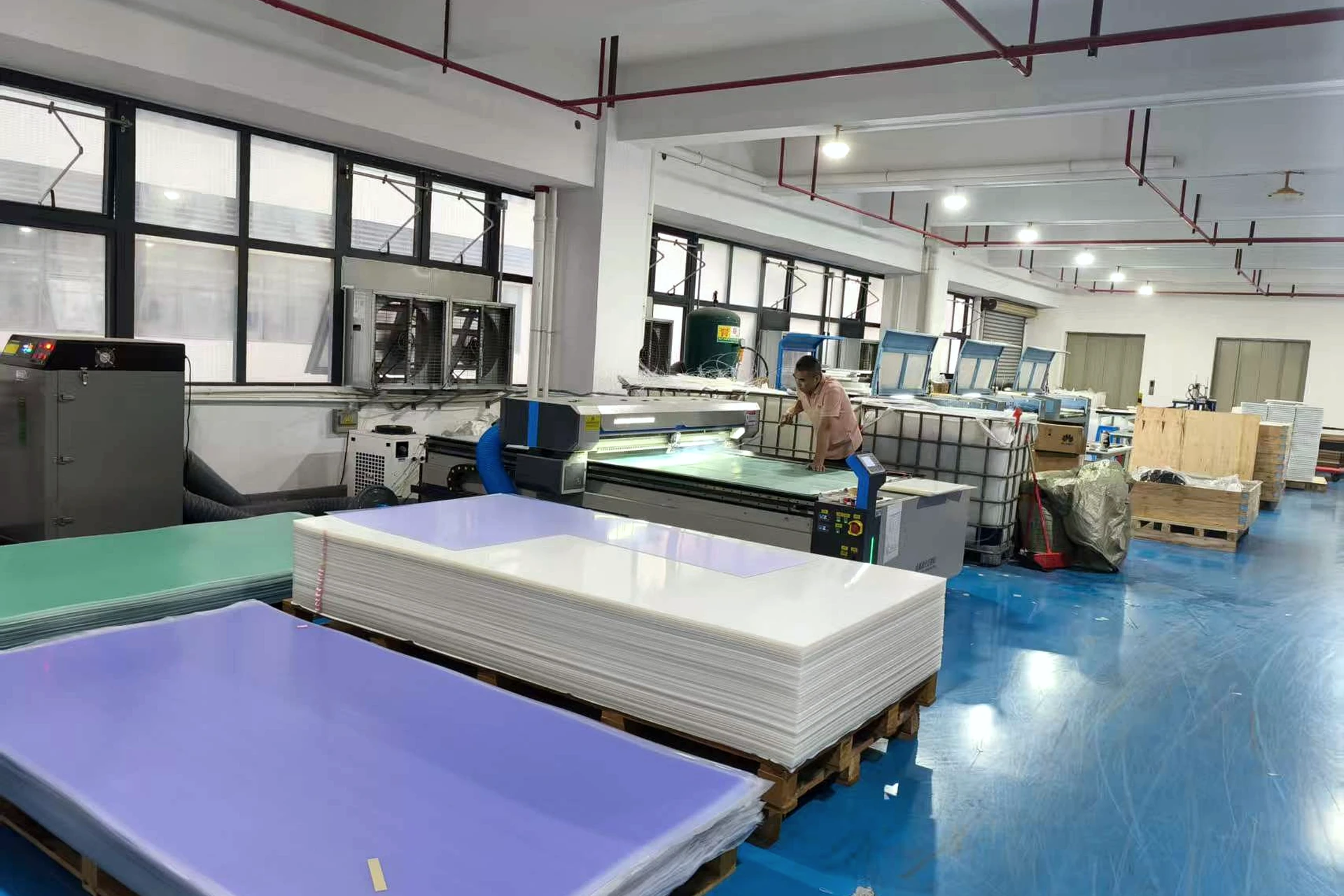 Operator working beside large-format equipment and stacked sheet material in a production area