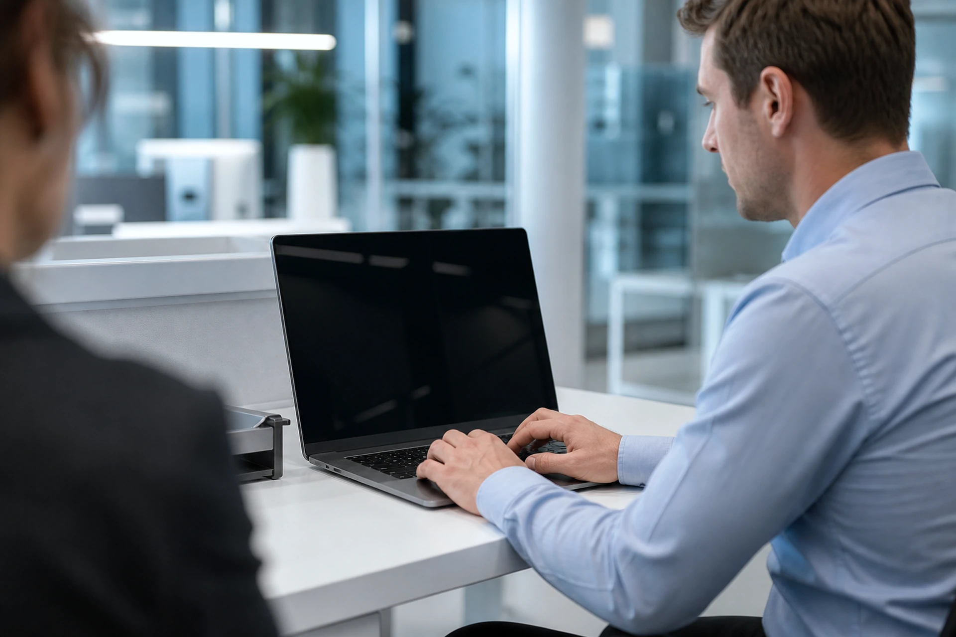 Side view of a business user working on a laptop whose screen appears dark to a nearby colleague