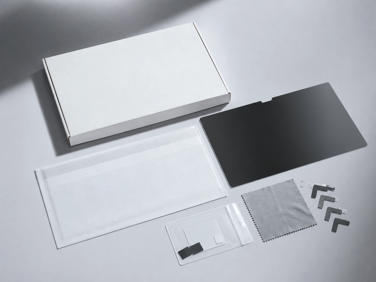 Privacy filter, protective sleeve, cloth and blank paperboard package arranged on a cool gray surface