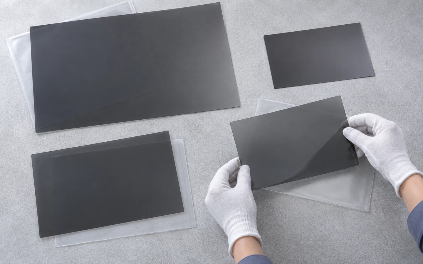 Gloved hands sort thin dark filter sheets of different sizes beside protective sleeves.